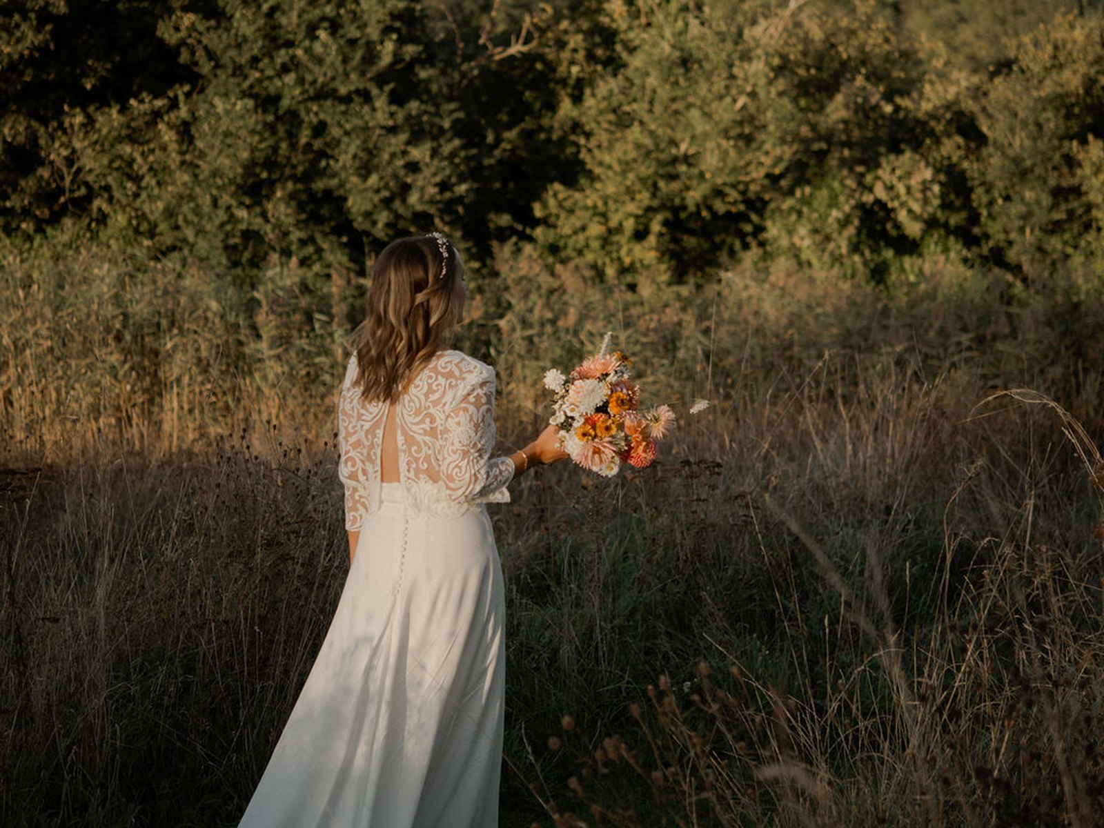 La mariée et son bouquet dans la prairie au soleil couchant